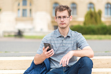 Obraz premium Young man sitting on the stairs with his phone