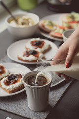 Breakfast with dark bread with white cheese and jam. Woman pouring milk for coffee
