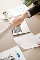 Close up of female and male shaking hands, businessman and businesswoman handshaking above office table with charts graphs after successful negotiations, partners concluding contract, top view