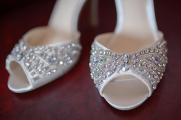 Cropped, white silk bridal peep toe shoes with rhinestones and delicate beads, displayed fully, in pair, on a dark red background