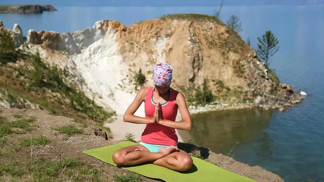 Young brunette professional yoga woman practices yoga moves outdoors. blue lake baikal on the background