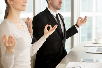 Close up view of business people meditating at desk, practicing pranayama technique to relax at office, holding hands in chin mudra gesture, corporate yoga, stress management for workspace wellness