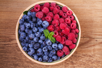 Blueberries and raspberries in clay bowl. Freshly picked berries on rustic background. Berry antioxidant superfood, concept for healthy eating. View from above, top studio shot