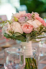 Vertical shot of elegant peonies, roses and silk bridal bouquet resting on a table at the reception venue, in a transparent vase