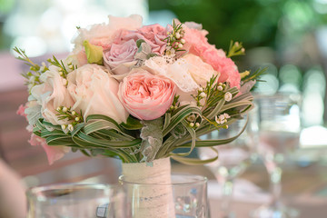 Horizontal shot of elegant peonies, roses and silk bridal bouquet resting on a table at the reception venue, in a transparent vase