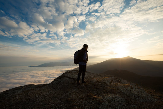 Silhouette of tourist hiker with backpack standing on the top of the mountain and looking at beautiful yellow autumn landscape sunset over clouds