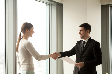 Happy businessman and businesswoman shaking hands while standing in office, satisfied partners reach agreement after effective successful negotiations, making sealing good deal, concluding contract