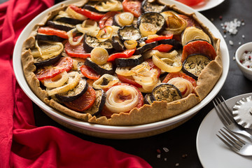 Homemade vegetable pie (galette) with grilled eggplants, tomatoes and onion on brown wooden background. Selective focus