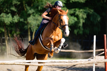 Young female jockey on horse leaping over hurdle