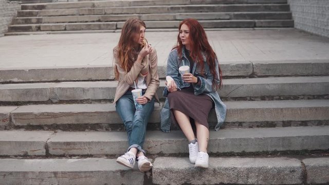 girls eating fast food sitting on steps in city