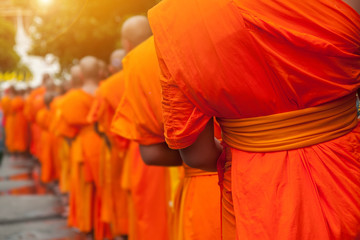 Buddhist philanthropy concept. Buddhist Monks line up in row waiting for Buddhism people to give alms bowl in Thai temple at morning time. Selective focus at front Monk. Light with len flare effect