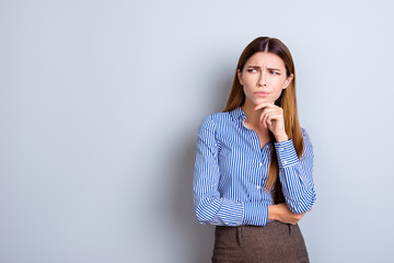 Sceptical young business lady is unsure what to do. She has focused grimace, wearing strict formal wear, standing on pure light background
