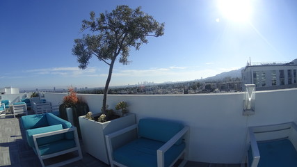 A rooftop lounge with blue sitting chairs, on the roof of a residential building, with a panoramic view of Los Angeles in the background.