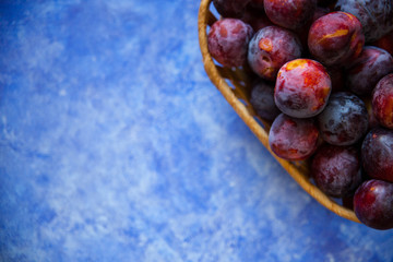 Overhead still life of purple plums in basket on blue textured background with copy space
