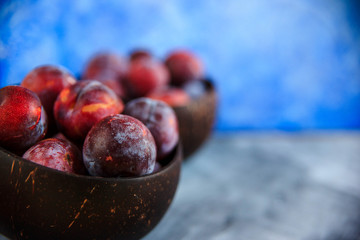 Still life of purple plums in basket on blue textured background with copy space