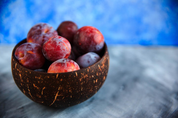 Still life of purple plums in basket on blue textured background with copy space