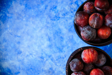 Overhead still life of purple plums in basket on blue textured background with copy space