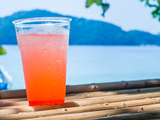 Plastic glass of cocktail on dry bamboo table and seascape.
