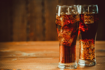 Beautiful cold fizzy cola soda with cubes ice in glasses goblet on old wooden background with free...