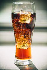 Beautiful cold drink of Cola with ice cubes in a glass on a grey window background with free space