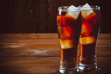 Beautiful cold fizzy cola soda with cubes ice in glasses goblet on old wooden background with free space