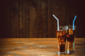 Beautiful cold drink of Cola with ice cubes with a boiler straws in glasses on wooden background with free space. Shallow DOF.