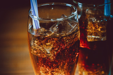 Beautiful cold drink of Cola with ice cubes with a boiler straws in glasses on wooden background with free space. Shallow DOF.