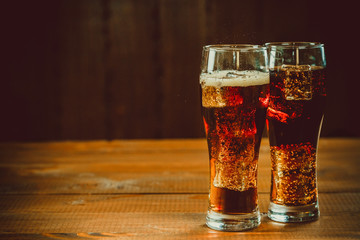 Beautiful cold fizzy cola soda with cubes ice in glasses goblet on old wooden background with free space. Shallow DOF.