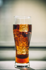Beautiful cold drink of Cola with ice cubes in a glass on a grey window background with free space. Shallow DOF.