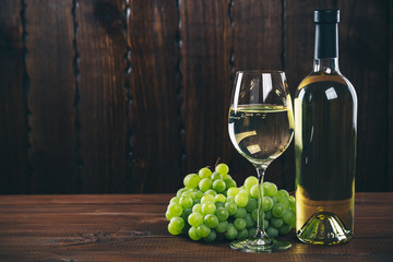 Beautiful White wine in wine glass with a bunch of green grapes, on a wooden background with free...