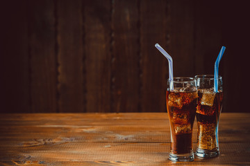 Beautiful cold drink of Cola with ice cubes with a boiler straws in glasses on wooden background with free space. Shallow DOF.