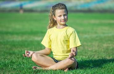 A young, pretty little girl doing yoga exercises. A child sitting in Lotus asana. Copy-space