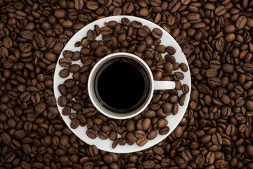 Top view of a coffee cup and a saucer filled with black coffee resting on cofee beans.