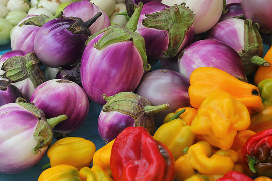 Eggplants, Bell Peppers And Onions On A Market Stand.