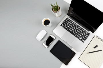 Office table with  laptop computer, notebook, digital tablet and smartphone on modern two tone (white and grey) background.