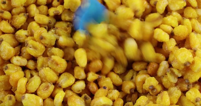 Close video of stirring toasted corn nuts with a small plastic blue spoon..