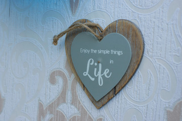 Heart-shaped wooden frame sign hang on the wall, which reads Enjoy the simple things in life