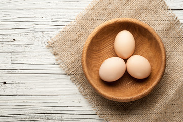 chicken eggs in wooden plate on white wooden background