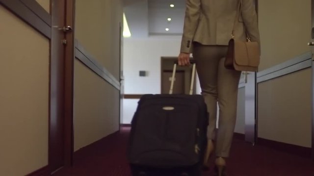 Slow motion rear view of businesswoman l walking through corridor with luggage in hotel