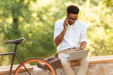 Handsome man using laptop computer talking by phone.