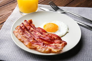 Plate with fried egg and bacon on table