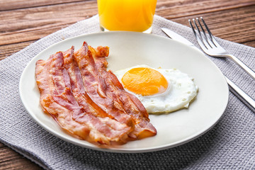 Plate with fried egg and bacon on table