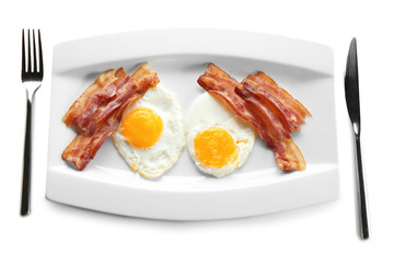 Plate with fried eggs, bacon and cutlery on white background