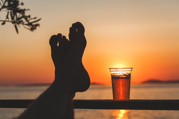 Man's feet and a beer cup with setting sun in the background