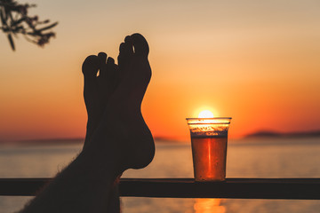 Man's feet and a beer cup with setting sun in the background