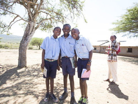 Smiling school boys with female teacher outdoors. Kenya, Africa.
