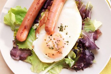 Plate of homemade fried egg, sausages and mix salad on table