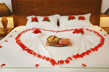 Bed with flowers and fruits in hotel room prepared for romantic date