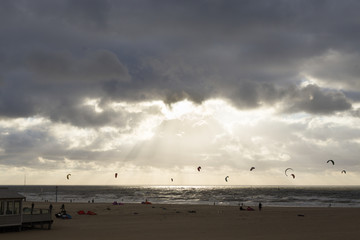 Kiteboarders in the sea and sun behind clouds atop