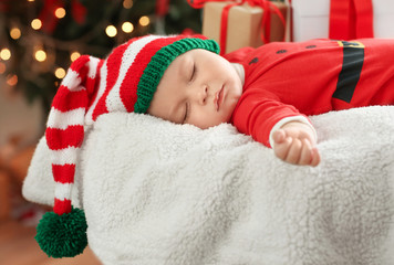 Cute little baby in Santa costume sleeping against blurred Christmas lights background